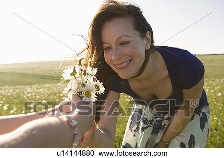Stock Image - Happy woman looks at wild flowers. Fotosearch