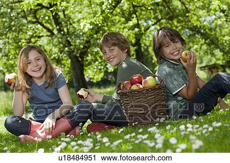 Stock Image - Kids in meadow, eating apples. Fotosearch