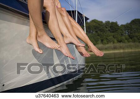 Stock Image - Legs hanging from boat. Fotosearch
