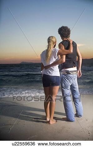 Stock Photograph - Loving cple look out to sea sunset. Fotosearch