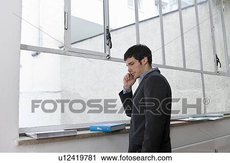 Stock Image - Man at window speaking on the phone. Fotosearch