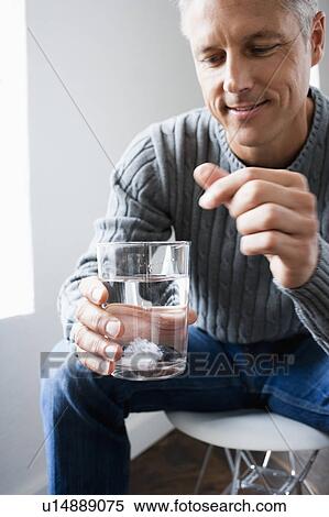 Stock Photography - Man dropping pill into glass of water. Fotosearch