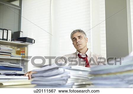 Stock Photo - Man in office with pile of paperwork. Fotosearch