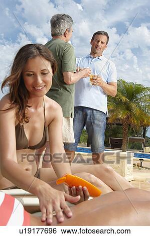 Stock Photograph - Man looking at woman applying sunblock. Fotosearch