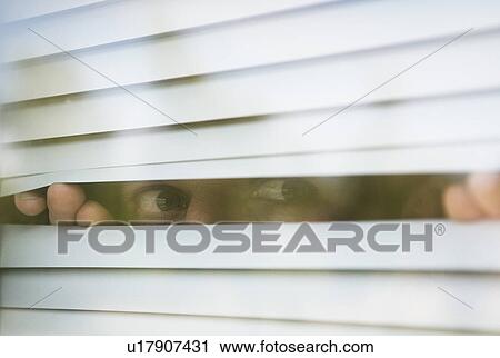 Stock Image - Man looks thru window blinds. Fotosearch