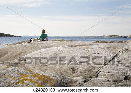 Stock Image - Man lying on rock and looking out to sea. Fotosearch