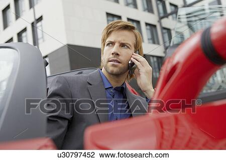 Stock Image - Man on phone in his electric sports car. Fotosearch
