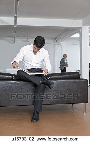 Stock Image - Man reviewing a book on the sofa. Fotosearch