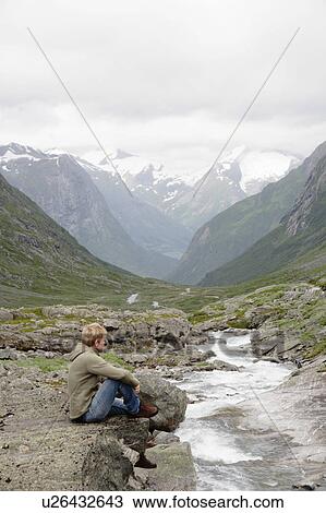 Man sitting by stream and mountains View Large Photo Image Stock Image - Man sitting by stream and mountains. Fotosearch