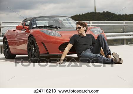 Stock Image - Man sitting in front of electric car. Fotosearch