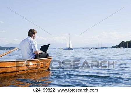 Man sitting on a rowboat using laptob View Large Photo Image Stock Image - Man sitting on a rowboat using laptob. Fotosearch