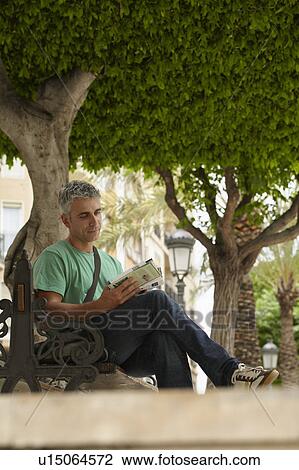 Man sitting on bench reading guidebook View Large Photo Image Stock Image - Man sitting on bench reading guidebook. Fotosearch
