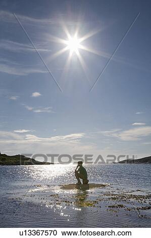 Stock Image - Man sitting on rock in sea. Fotosearch