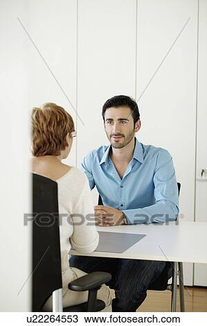 Stock Image - Man sitting opposite woman in office. Fotosearch