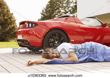 Stock Photography - Man sleeping next to his electric car. Fotosearch