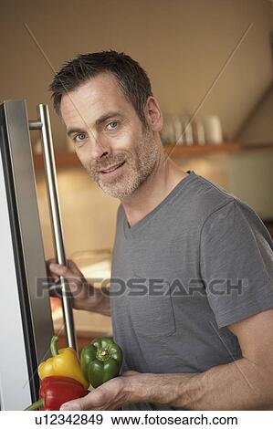 Stock Photo - Man standing in front fridge. Fotosearch