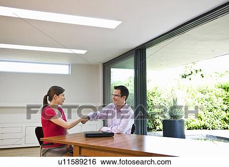 Stock Photograph - Man & woman shake hands over table. Fotosearch