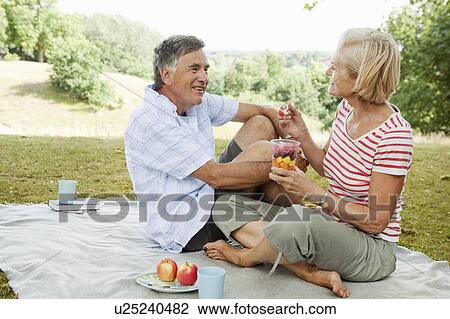 Stock Image - Mature couple having picnic in park. Fotosearch
