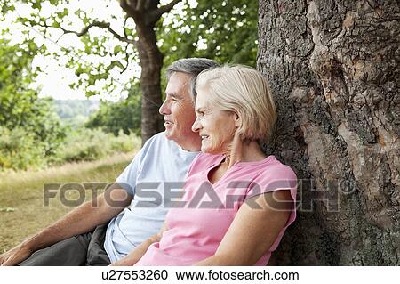 Stock Image - Mature couple sitting against tree. Fotosearch