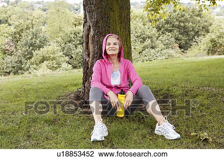 Mature woman sitting against tree View Large Photo Image Stock Image - Mature woman sitting against tree. Fotosearch
