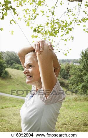 Picture - Mature woman stretches arm in park. Fotosearch