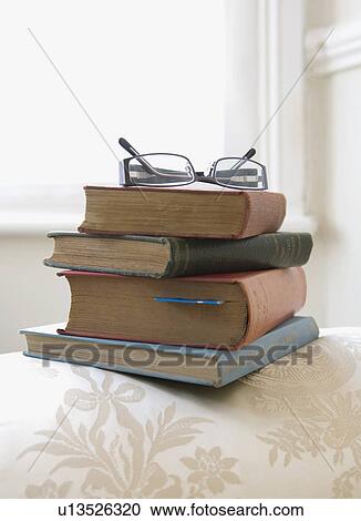 Stock Image - Pile of books on arm of sofa. Fotosearch