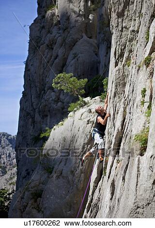 Stock Image - Rock climber climbing rock face. Fotosearch