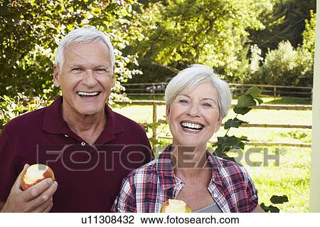 Stock Image - Senior couple eating apples smiling. Fotosearch