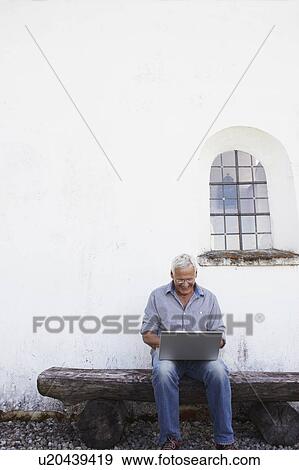 Senior man sitting at bench with laptop View Large Photo Image Stock Photo - Senior man sitting at bench with laptop. Fotosearch