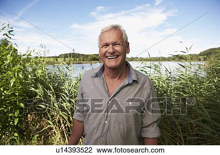 Stock Image - Senior man standing in front of lake. Fotosearch