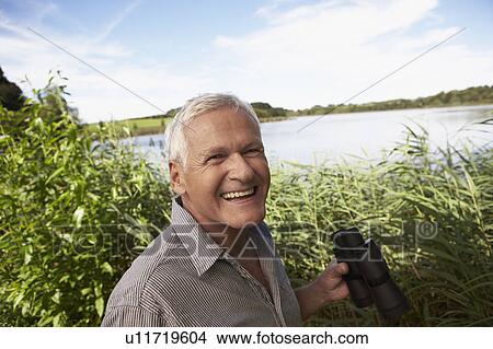 Senior man with binoculars in front lake View Large Photo Image Picture - Senior man with binoculars in front lake. Fotosearch