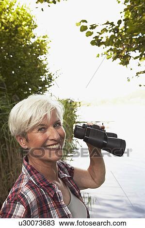 Stock Image - Senior woman holding binoculars. Fotosearch