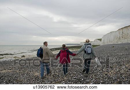 Stock Image - Seniors and grandchild walk on beach. Fotosearch