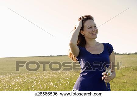 Stock Photograph - Smiling woman holds flowers in meadow. Fotosearch
