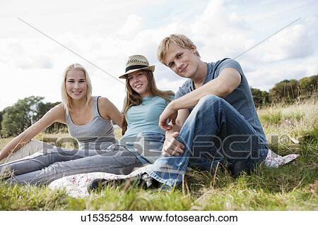Picture - Three young persons sitting in grass. Fotosearch