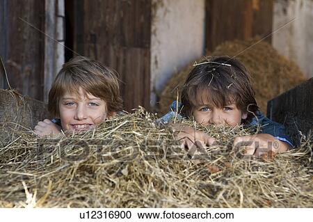 Stock Image - Two boys hiding in hay, happy. Fotosearch