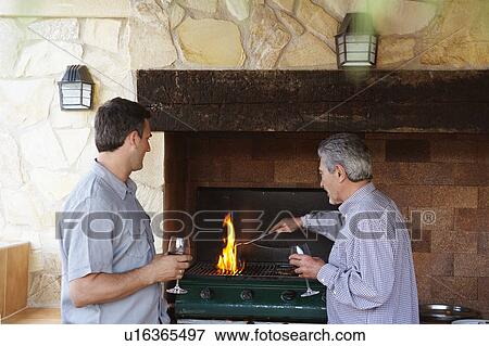 Stock Photo - Two men by barbeque holding wine glasses. Fotosearch