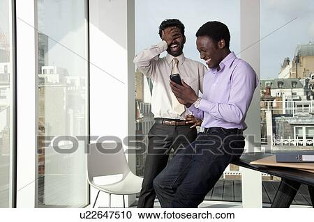 Stock Image - Two men laughing at telephone display. Fotosearch