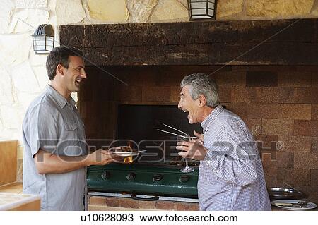 Stock Image - Two men laughing together by barbeque. Fotosearch