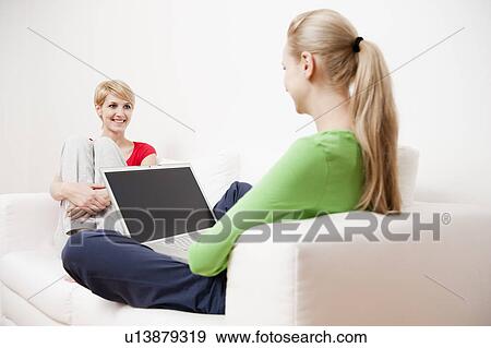 Two women using laptop and phone on sofa View Large Photo Image Stock Photo - Two women using laptop and phone on sofa. Fotosearch