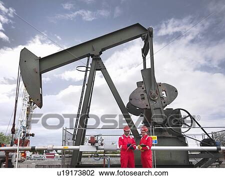Two workers in front of oil well pump View Large Photo Image Stock Image - Two workers in front of oil well pump. Fotosearch