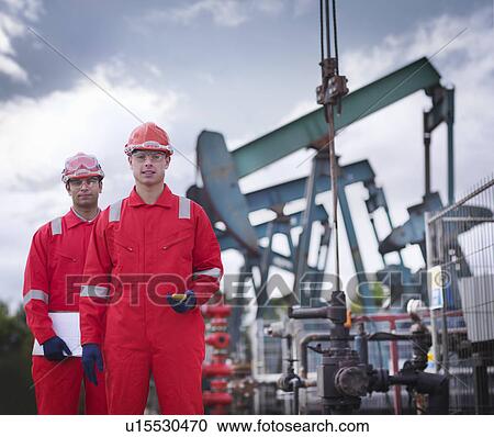 Stock Image - Two workers in front of oil well pumps. Fotosearch