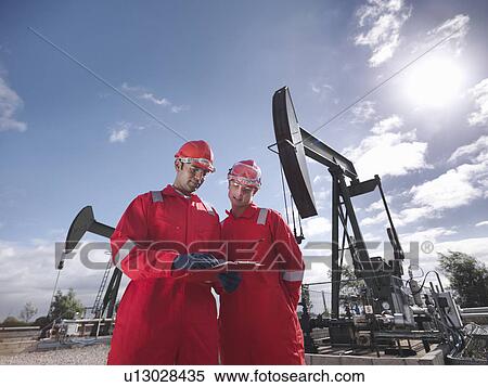 Stock Photography - Two workers in front of oil wells. Fotosearch