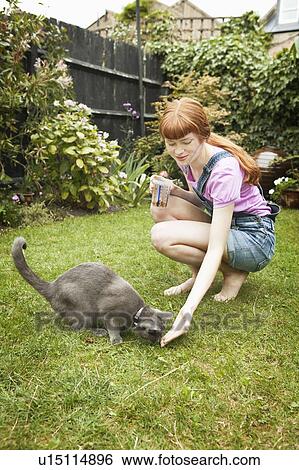 Stock Photograph - Woman feeding cat in garden. Fotosearch