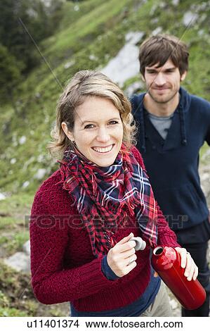Woman holding bottle man in background View Large Photo Image Picture - Woman holding bottle man in background. Fotosearch