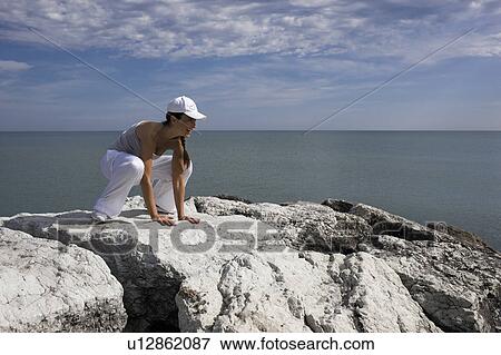 Stock Photo - Woman hunkering down on rocks. Fotosearch