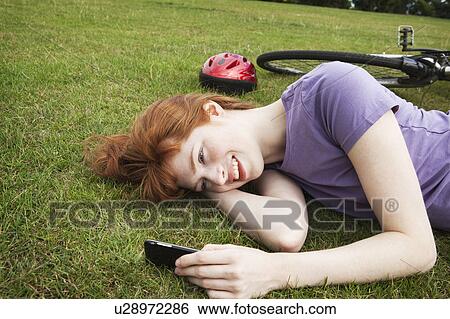 Stock Photograph - Woman laying in grass, texting. Fotosearch