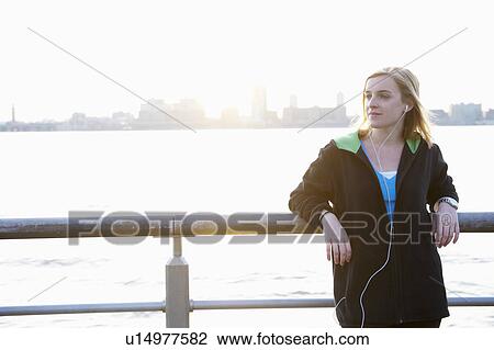 Stock Image - Woman leaning against a fence, with ipod. Fotosearch