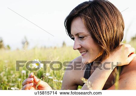Picture - Woman looking at daisy. Fotosearch