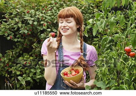 Stock Image - Woman looking at homegrown strawberry. Fotosearch